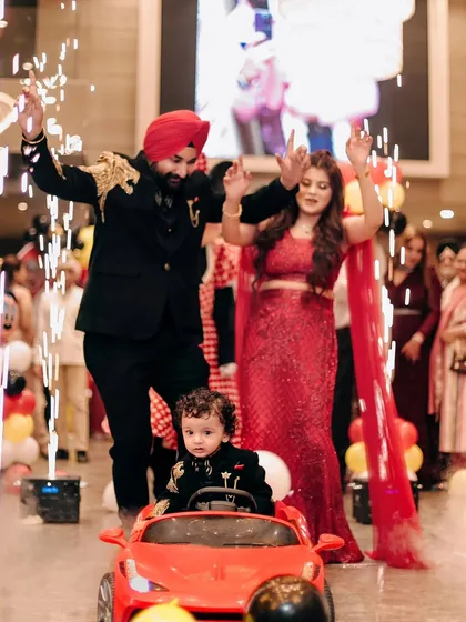 Making a grand entrance at his birthday party. This little boy arrives in style in a red toy car, surrounded by sparklers and his cheering parents.