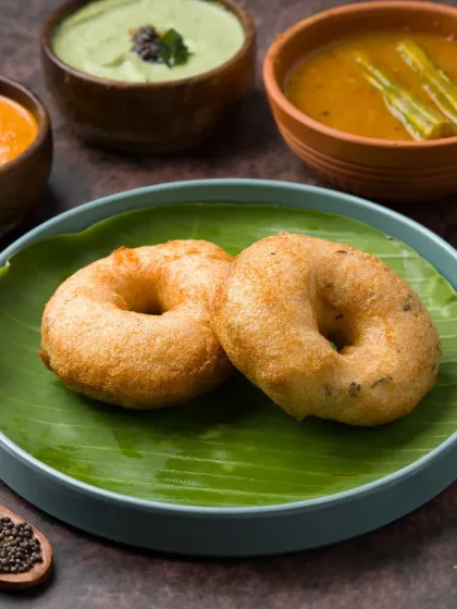 A classic Medu Vada shot, styled traditionally on a banana leaf with accompanying chutneys and sambar. This type of authentic presentation helps build trust and appeal for South Indian restaurants.