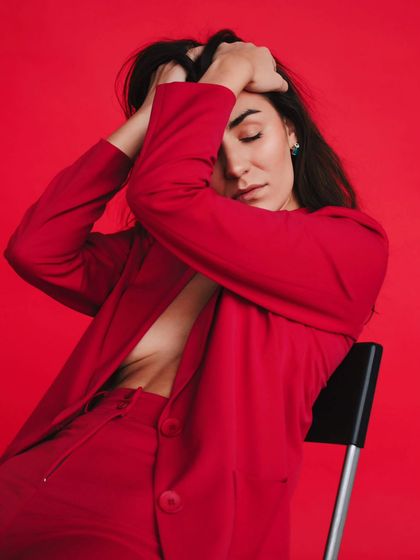 A powerful and emotive pose against a solid red background. This portrait is all about conveying strength and passion through body language.