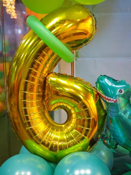 Details matter. A close-up of the large number '6' foil balloon and a T-Rex balloon, part of the intricate decorations for a 6th birthday party.