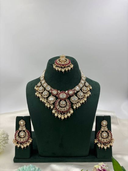 A heavy Moissanite Kundan bridal set in a rich ruby red, displayed on a mannequin to show its full form.