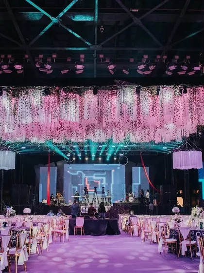 A grand overview of Tanisha and Neel's psychedelic-themed Sangeet. The space is dominated by a massive floral and fringe installation hanging from the ceiling, with vibrant pink lighting and modern lounge seating below.