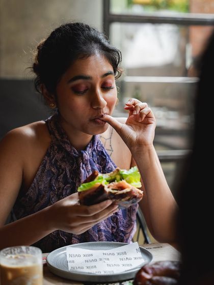 A customer enjoying a bite of a bagel sandwich, savoring the flavor. It's finger-lickin' good.