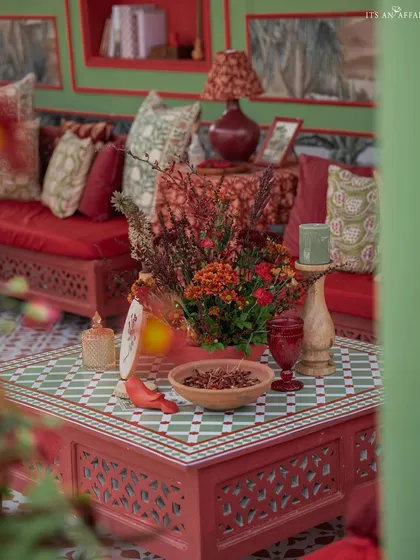 A detailed shot of a coffee table, featuring a custom tile-top, rich red floral arrangements, and traditional Indian decor pieces. Every detail is curated to fit the Mughal theme.