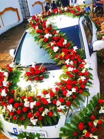 A heavy floral decoration for a white car, using a garland of red and white flowers that sweeps across the hood.