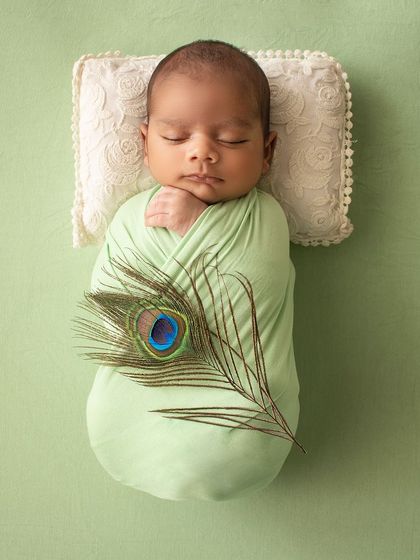 A simple and meaningful portrait. This newborn is swaddled in green with a single peacock feather, a nod to Indian culture.
