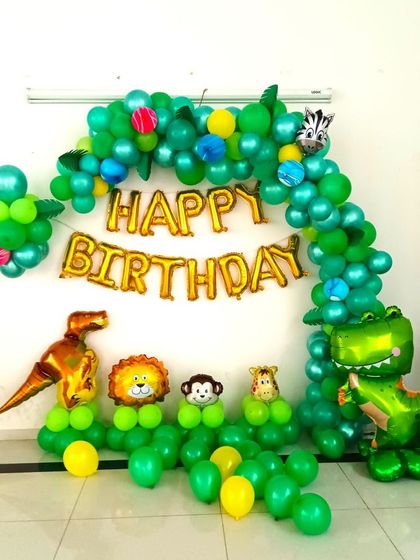 A simple jungle theme birthday decoration for a home party. The setup uses a green balloon arch with animal foil balloons to create a fun and festive atmosphere.