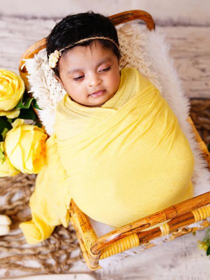 A close-up of a sweet newborn wrapped in a yellow swaddle, resting in a wooden prop with matching flowers.