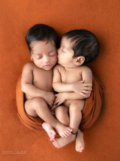 A beautiful portrait of newborn twins, with one giving the other a gentle kiss on the cheek. This image perfectly captures the pure magic and love of their bond.