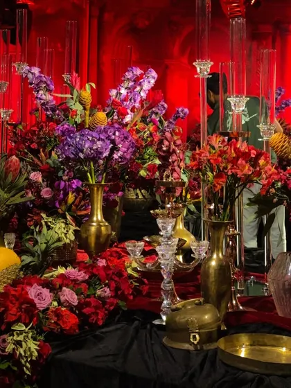 A lush corner of the Siddartha Tytler set, showcasing a rich mix of purple, red, and orange blooms in brass vases. This layering of color and texture is a signature of my maximalist designs.