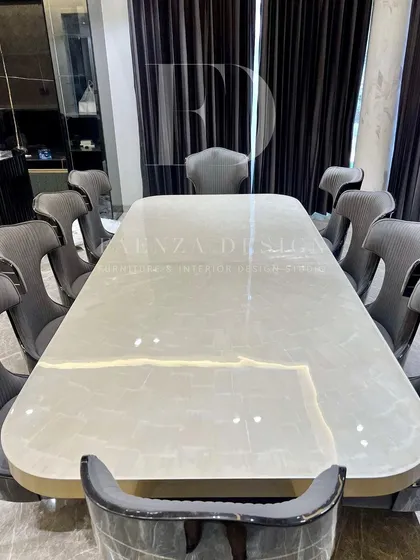 An opulent 10-seater dining set. The table features a lustrous white onyx top with a brass-trimmed base, surrounded by high-back chairs with unique cut-out details and dual-fabric upholstery.