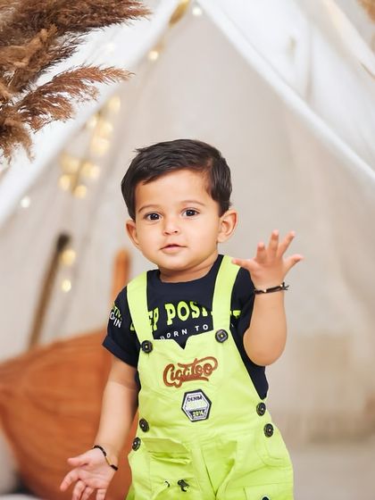 A close-up of a curious toddler during a boho-themed outdoor shoot. The combination of natural greenery and styled props like the teepee and pampas grass creates a unique look.