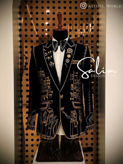 This tuxedo jacket on a mannequin features intricate gold embroidery inspired by ancient hieroglyphics. It's a unique fusion of history and modern tailoring for a truly distinctive look.