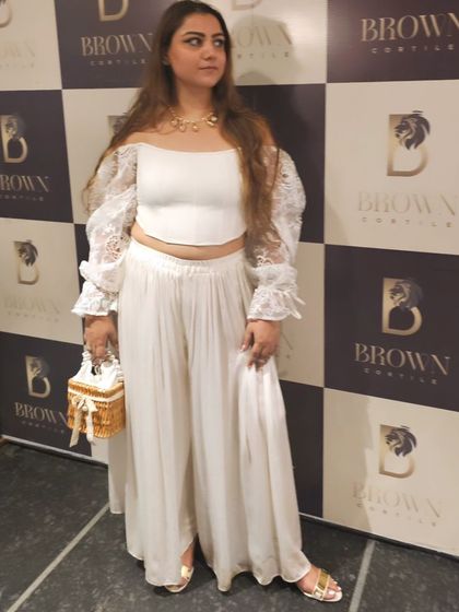 Another pose from 'The White Party'. The off-shoulder top with lace sleeves and flowing pants creates an elegant silhouette, perfectly finished with our accessories.