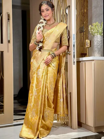A full-length portrait of the South Indian bride, looking like a goddess in her golden saree. The makeup is kept luminous and warm to complement the traditional attire and intricate jewelry.