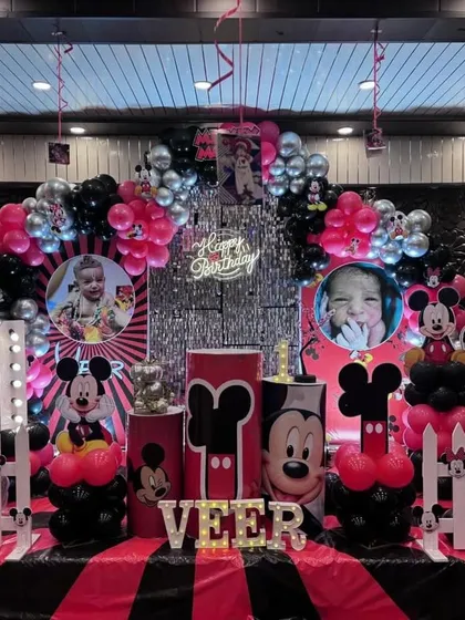 A classic Mickey Mouse theme for a first birthday. The decor includes a custom backdrop, Mickey-themed pedestals, and a black, red, and silver color scheme.