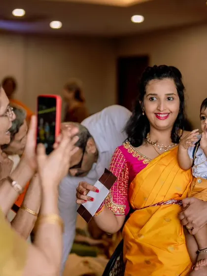 Capturing memories at a family event. This candid photo shows a mother holding her baby, who is the center of attention, at what looks like a naming ceremony or birthday party.