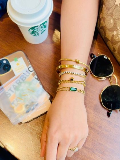 A flatlay-lifestyle hybrid, this shot features a model's arm stacked with bracelets alongside cafe-themed props like a coffee cup and sunglasses. It creates a complete visual story for a social media post.