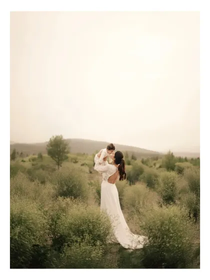 A mother in a flowing white dress lifts her child high in a field of wildflowers. This image captures the boundless love and freedom of motherhood, a moment of pure magic captured with natural light photography.