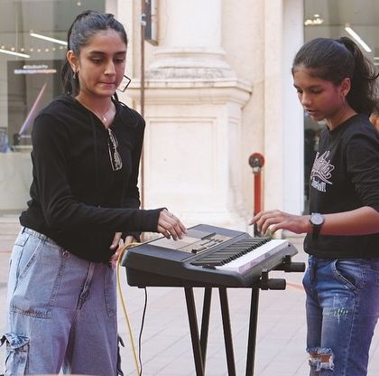 A teacher assists a student with her keyboard setup during a soundcheck for a live show. We ensure our performers are prepared and confident before they go on stage.