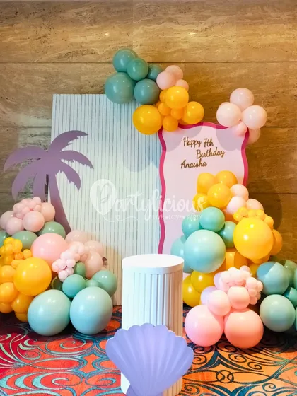 A closer look at our beachy, tropical decor. This setup for a 7th birthday features a custom backdrop with a palm tree silhouette and a cascade of pastel balloons, creating a chic and sunny vibe.