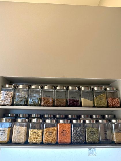 A wide cabinet with two long shelves full of perfectly organized dals and grains. This panoramic view shows the satisfying impact of a fully implemented pantry system.