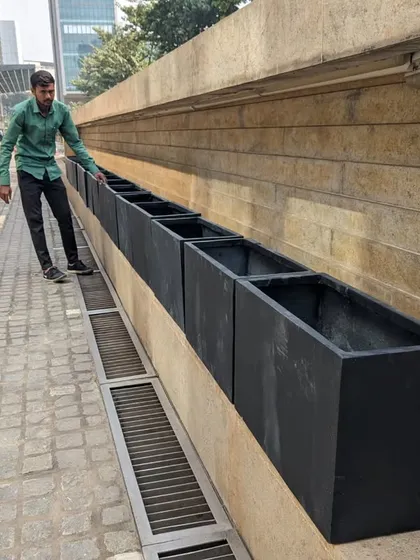 I am inspecting the placement of the black rectangular FRP planters along the building's foundation. Proper alignment is key to achieving the sleek, uniform look required for this corporate landscaping project.