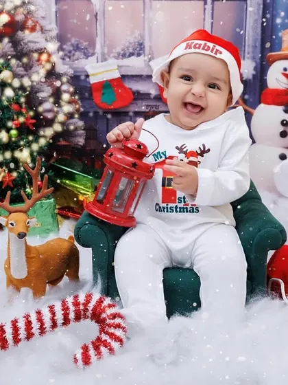 This baby's first Christmas is full of smiles! He's sitting in our festive setup with a Christmas tree, reindeer, and a personalized Santa hat.