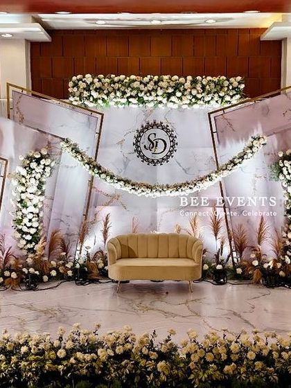 A full view of a modern and sophisticated reception stage. The design uses clean lines, a marble-patterned backdrop, and lush arrangements of white flowers and pampas grass for a contemporary yet timeless feel.