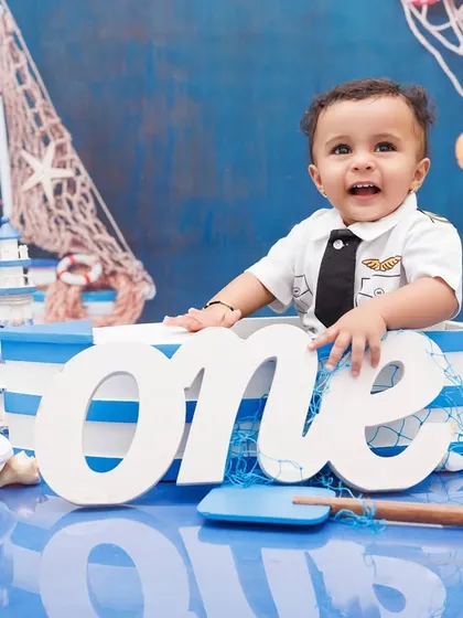Ahoy, captain! A smiling one-year-old in a nautical-themed setup, complete with a boat and captain's hat.