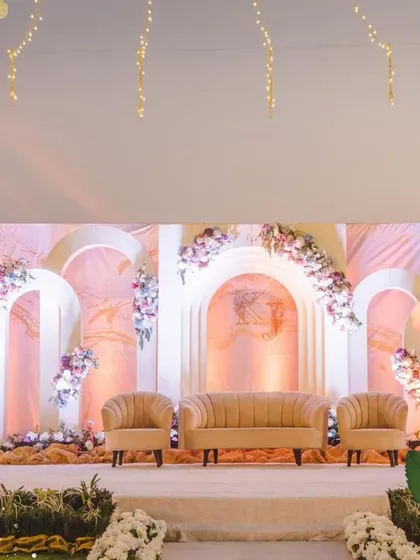 The stage setup for an engagement party, featuring a soft, romantic design. The backdrop consists of elegant arches in pastel tones, adorned with asymmetrical floral arrangements, creating a modern and sophisticated look.