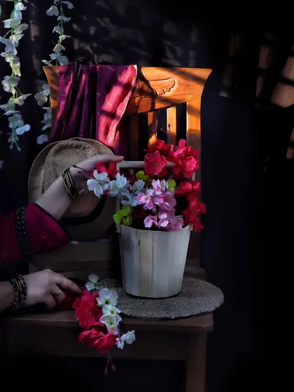 A still life composition featuring a wooden bucket of colorful flowers on a chair, with dramatic shadows from a window. This image shows how I play with light and shadow to create artistic photos.