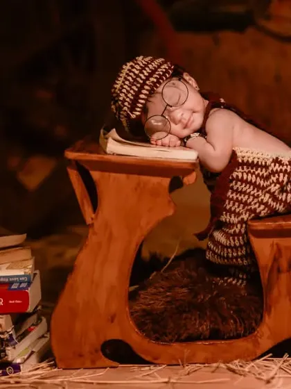 A charming newborn photo with a baby in a hand-knitted outfit, asleep on a tiny wooden desk, perfect for a 'future scholar' theme.