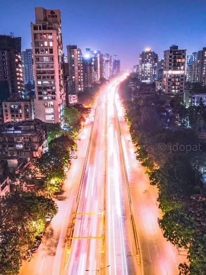 A long-exposure photograph of a main road in Mumbai at night, where the light trails from traffic flow like a river of light through the city.