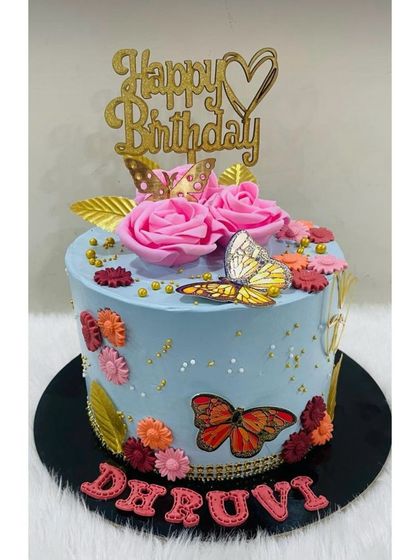 A beautiful blue cake adorned with pink roses, golden leaves, and colorful butterflies, creating a vibrant and graceful design.