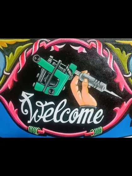 A close-up of the "Welcome" banner on the Iron & Gold Tattoo sign, featuring a hand holding a tattoo machine.