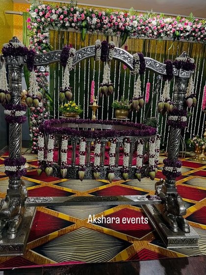 A grand silver cradle, intricately decorated with purple and white flowers, set against a backdrop of hanging jasmine garlands. This is a classic and elegant choice for a naming ceremony.