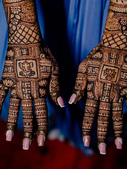 A powerful design featuring auspicious symbols. One hand has a Ganesha motif and the other has a lotus, both surrounded by swastika patterns, perfect for religious ceremonies and weddings.