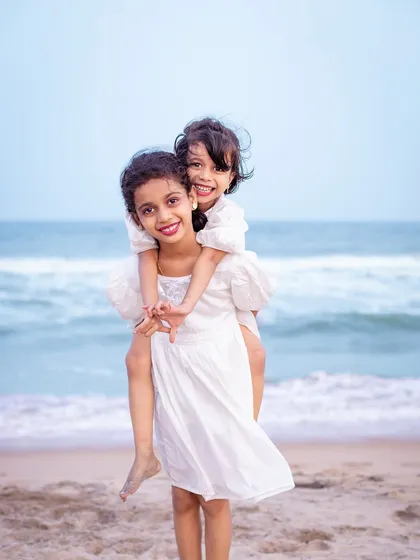 A sweet piggyback ride by the sea. This playful portrait of two sisters showcases their loving bond and the simple joys of a day spent at the beach, creating a cherished memory for their family.