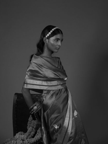 A classic black and white portrait that emphasizes form and emotion. By removing color, we draw attention to the elegant drape of the saree, the delicate headband, and the model's contemplative expression. This timeless approach is perfect for creating sophisticated brand imagery.