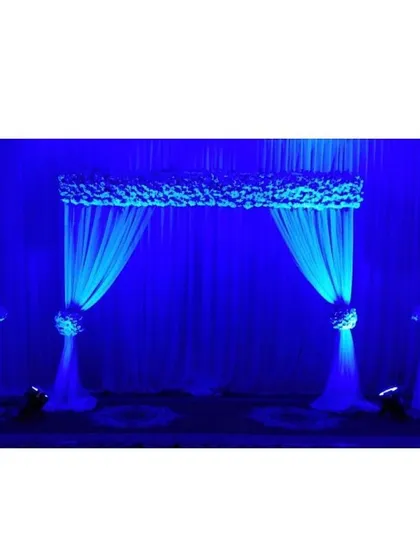 A simple and elegant entrance arch or stage backdrop created with drapes and florals. The deep blue lighting transforms the setup, proving that a simple design can have a powerful impact with the right lighting.