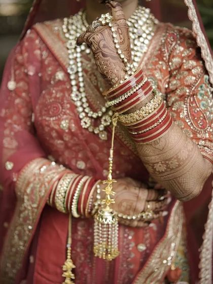 A close-up of the bride's hands, adorned with mehendi, traditional red bangles, and golden kaleere. This is the quintessential bridal look.