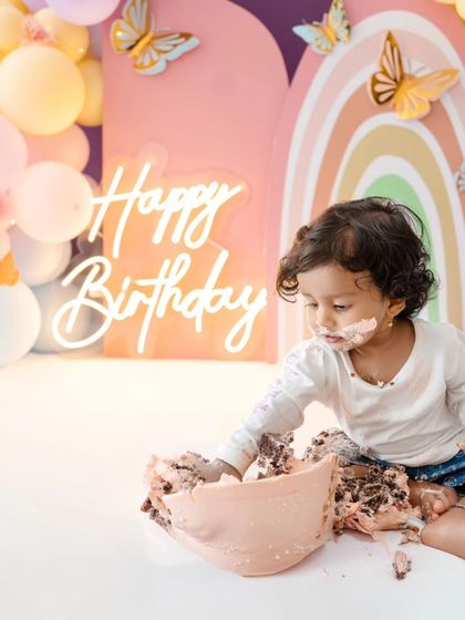 A dynamic shot of the cake smash in progress, showing the baby's hands covered in frosting.