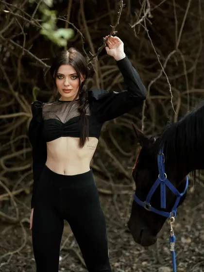 A model poses with a black horse against a backdrop of tangled branches, creating a raw and mysterious atmosphere. Our varied landscapes include wooded areas for more dramatic shoots.