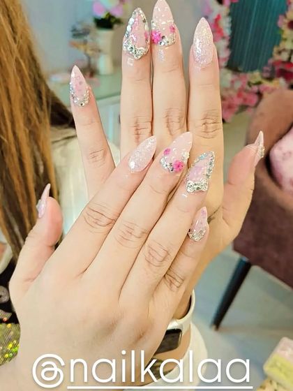 A dazzling set of long stiletto nails perfect for a bride or special occasion. It combines a soft pink glitter base with intricate silver rhinestone patterns and delicate 3D pink flowers.