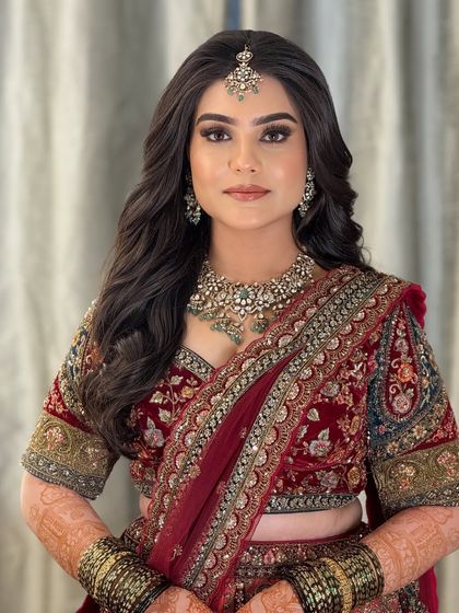 A stunning reception look in a deep red velvet lehenga. The makeup is glamorous and bold, with a smoky eye and a defined brow.