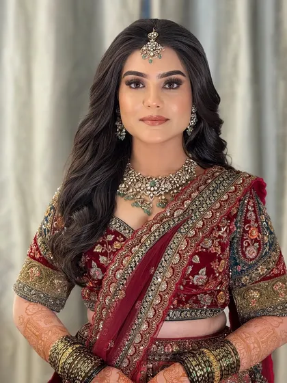 A stunning reception look in a deep red velvet lehenga. The makeup is glamorous and bold, with a smoky eye and a defined brow.