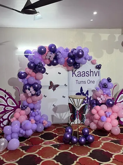 A full view of the purple and pink butterfly birthday backdrop. The setup features two large wing-shaped balloon arrangements flanking a personalized central panel.
