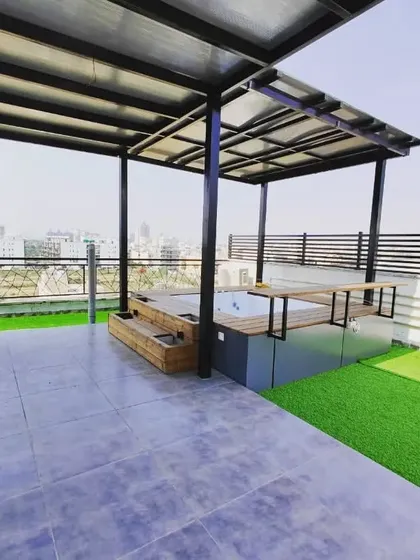 An open-air jacuzzi on a terrace, surrounded by a thermopine wood deck and covered by a sleek metal pergola.