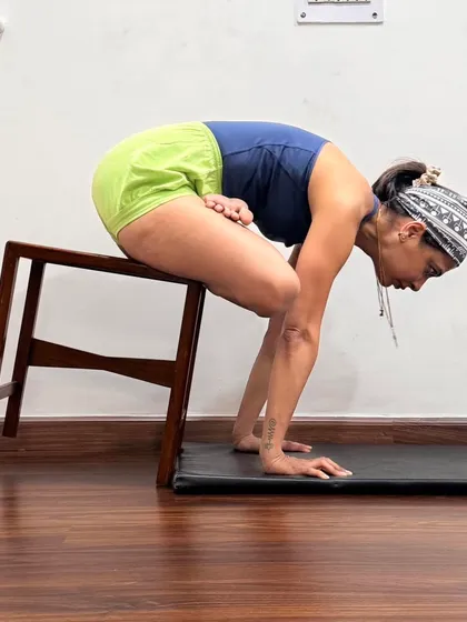 Urdhva Kukkutasana (Upward Cock Pose) is an advanced arm balance that requires core strength and hip flexibility. Here, it is practiced with the support of a stool to help with balance and alignment.